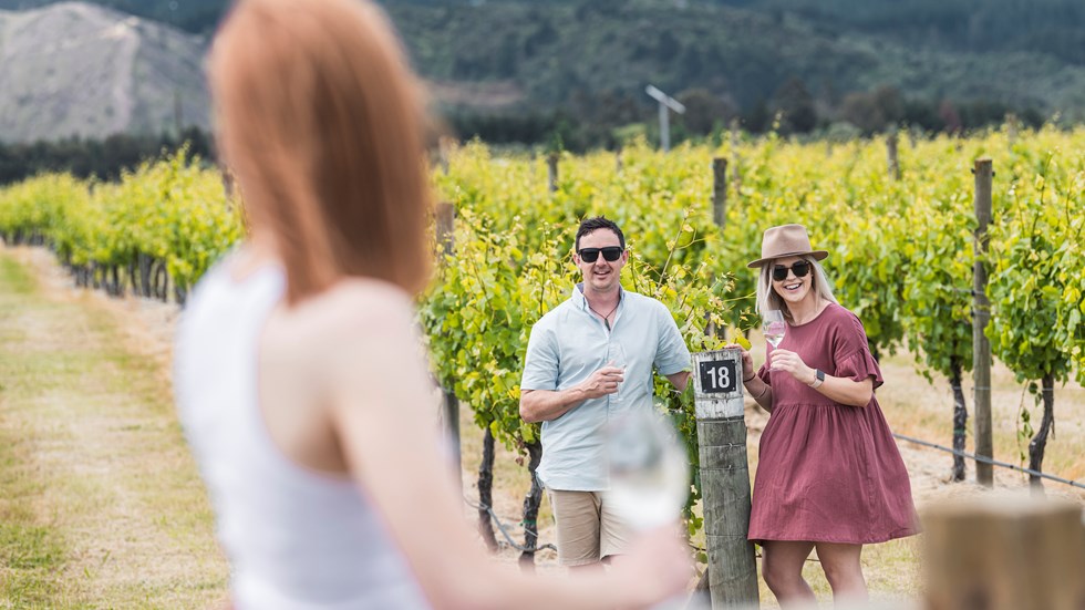 Three people drinking wine in a vineyard as part of a wine tour in Marlborough near Blenheim, at the top of New Zealand's South Island